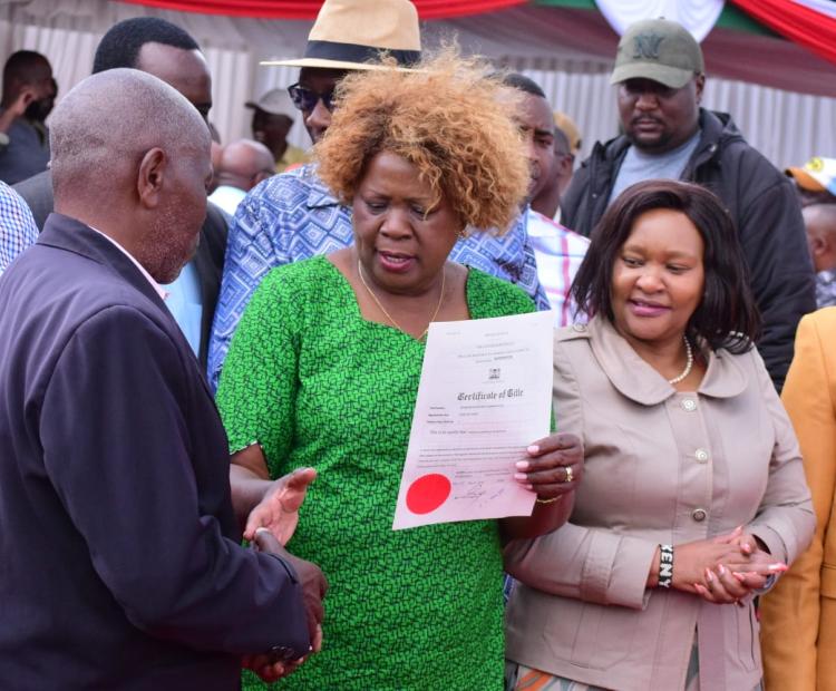 Lands Cabinet Secretary Alice Wahome (centre) hands over a title deed to a beneficiary in Ol Kalou, Nyandarua County. She issued 2,700 title deeds to residents of the area